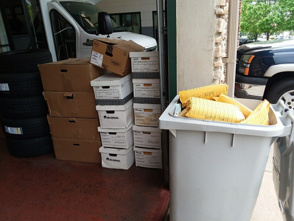 A secure collection container beside stacked bankers boxes full of files to be shred