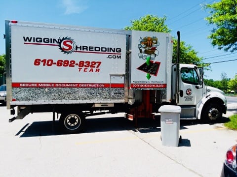 The Wiggins Mobile Shredding Truck in a parking lot with one secure collection containers beside.