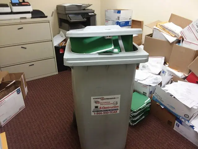 Secure Collection container full of documents in a messy office surrounded by other documents on the floor and in boxes