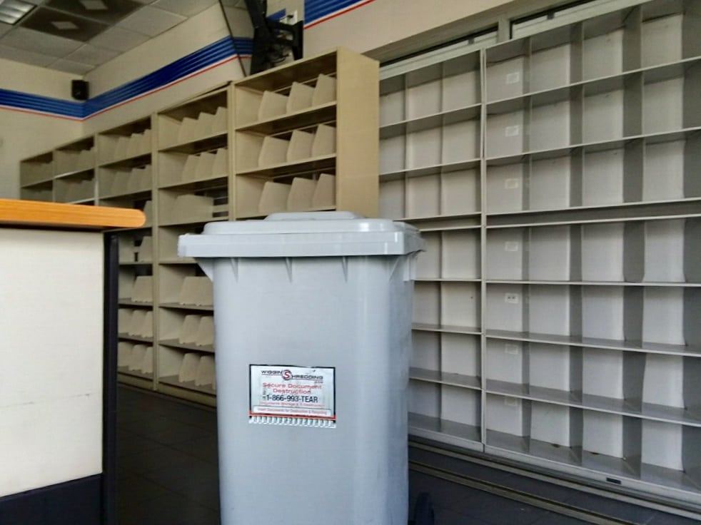 A secure shredding container in front of a wall of empty shelves