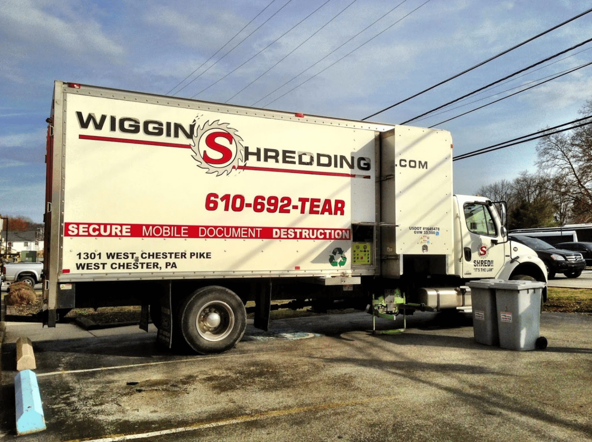 Wiggins shredding truck in parking lot with two secure collection containers beside