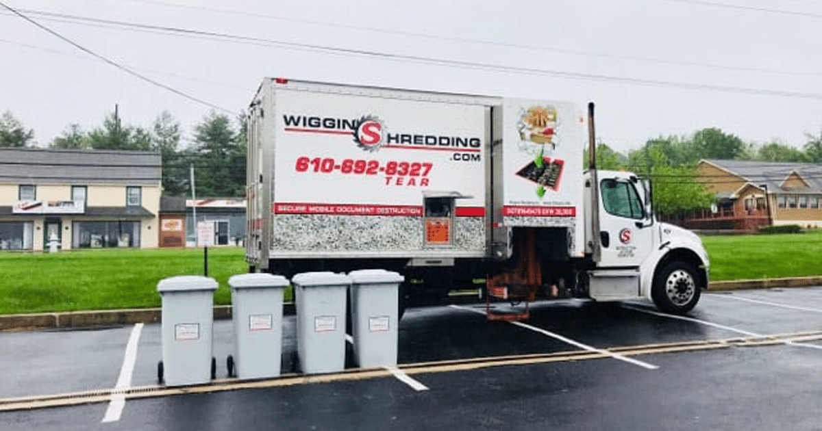 The Wiggins Mobile Shredding Truck in a parking lot with four secure collection containers beside.