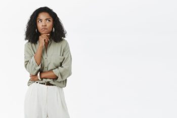 A woman standing against a white background making a thinking face