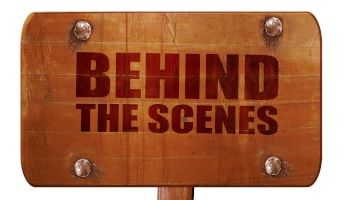 A wooden sign that reads Behind the Scenes
