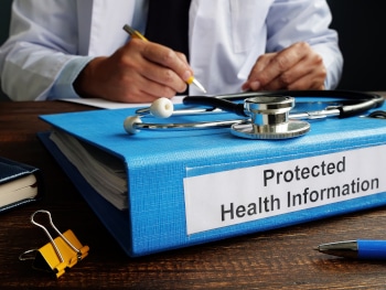 A doctor sitting a desk with a binder labelled "Protected Health Information