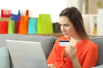 A woman looking confused at a laptop while holding a credit card