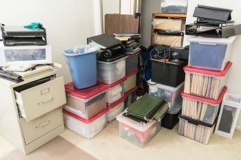 Cluttered corner in a work space with storage boxes, binders and miscellaneous office supplies