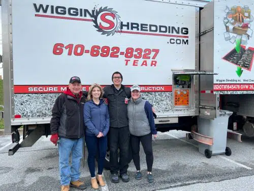 Four people posing outside in front of a Wiggins Mobile Shredding truck