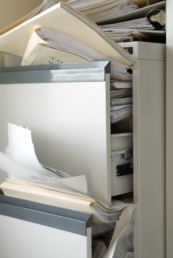 Closeup photo of a file cabinet filled beyond capacity and overflowing with files and papers