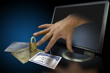 Image of a hand coming out of a computer monitor and reaching for credit cards and a Social Security Card laying in front of the screen.
