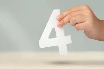 A hand holding up a piece of plastic in the shape of a number 4