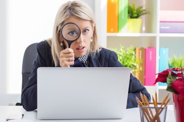 Woman looking through a magnifying glass while sitting in front of computer