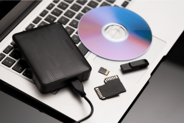 A laptop with a portalbe hard drive, CD/DVD, SSD cards, and a USB drive on its keyboard