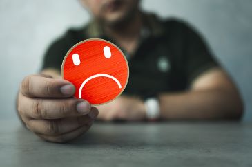 A person reaches forward across a table and holds out a circular card with a red sad face emoji.