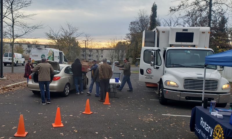 During an outdoor shred event in the fall, people are moving boxes from the trunk of a car to a mobile shredding truck.