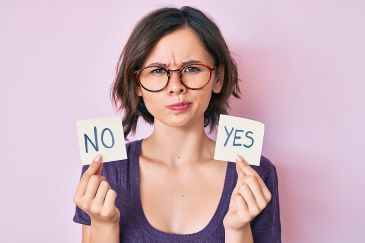 Young woman looking skeptical is holding up both a "yes" and a "no" sign.